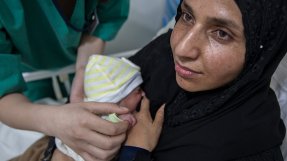 En nybliven mamma på Rafik Hariri sjukhus i Beirut, Libanon, har sitt barn tätt intill bröstet, sjukvårdpersonal står lutad över sängen med en hand på barnet.