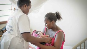 En anställd från Läkare Utan Gränser i Likoni, Kenya, står brevid en nybliven mamma som sitter på en säng. I famnen håller kvinnan sitt barn.