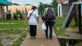 En anställd från Läkare Utan Gränser går med ryggen mot kameran bredvid en man med ryggsäck i byn Bajo Chiquito i Panama.