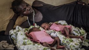 En mamma ligger på en sjukhussäng aå Aweil-sjukhuset i Sydsudan och tittar på sina nyfödda tvillingar som ligger framför henne på sängen.