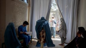 En korridor på vår undernäringsklinik i Herat, Afghanistan. På bilden syns tre kvinnor samt en personal som sitter på en bänk. I förgrunden är en vakt som öppnar en grind.