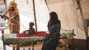 Ett litet barn sitter på en säng på en undernäringsklinik i Afarregionen, Etiopien. På bilden finns också två kvinnor som ser om barnet. 