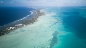 En smal landremsa med byggnader och träd på sig. Omkring ön är havet klarblått.