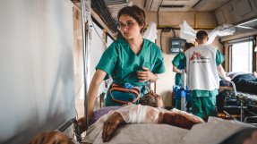 En patient med bandage på armen ligger på en bår och blir omhändertagen av en sjuksköterska