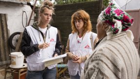 Två kvinnor i Läkare Utan Gränser västar pratar med en äldra kvinna. 