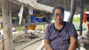 En kvinna sitter på en stol utanför sitt hus.