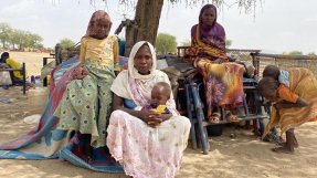 en kvinna sitter med sina barn på marken vid ett träd