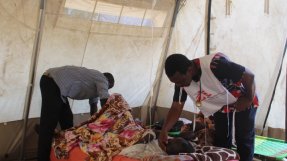 en patient ligger på en säng och omhändertas av personal på en vårdmottagning i ett flyktingläger i Tchad