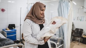 en barnmorska håller en nyfödd bebis insvept i vitt tyg på en mödravårdsavdelning