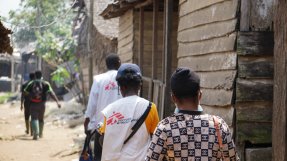 ett team från Läkare Utan Gränser går längs en bygata kantad av omålade trähus