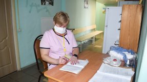 Kvinna i rosa t-shirt sitter vid skrivbord och antecknar i block.