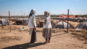 Två kvinnor står och kollar ut över ett flyktingläger.