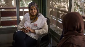 Kvinna med sjal och MSF-väst pratar med patient.
