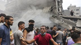 en samling människor vid en sönderbombad byggnad i Gaza