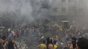 människor och en grävmaskin på en gata med sönderbombade byggnader