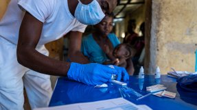 En manlig sjuksköterska men munskydd och plasthandskar undersöker ett malariatest på ett blått bord
