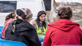 En grupp kvinnor, varav en har gul väst, sitter utomhus och pratar.