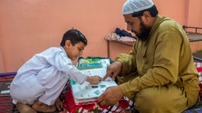 En pappa och hans son sitter mittemot varandra och tittar i en skolbok. 