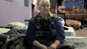 en äldre kvinnar sitter på en tältsäng i en stor sal