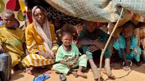 Kvinna och flera barn sitter i ett tält byggt av pinnar och tygstycken