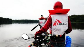 Två personer transporterar motorcyklar i en kanot över floden.