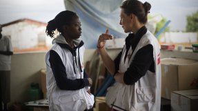 Två kvinnor i vita västar med Läkare Utan Gränsers logotyp står och pratar med varandra.