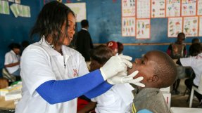 En kvinnlig vårdanställd med skyddshandskar ger ett barn ett oralt vaccin.