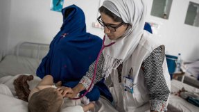 En kvinnlig läkare lyssnar på ett barns andning på ett sjukhus i Afghanistan.Bredvid på sängen sitter en anhörig kvinna med ansiktet täckt av en slöja. 