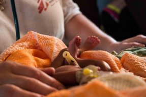 Ett nyfött barn insvept i en filt ligger framför en anställd på en klinik i Sydsudan