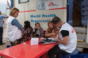 Tre patienter får vård av två läkare framför vår mobila klinik