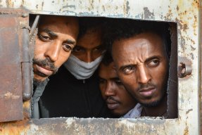 Fyra män tittar ut från ett förvar i Libyen.