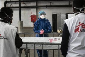 En kvinna i skyddskläder pratar med två män.