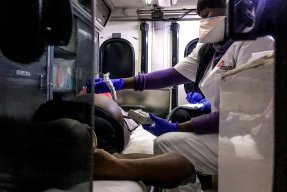 En kvinna gör ett ultraljud på en gravid kvinna som ligger på en bår i en ambulans.
