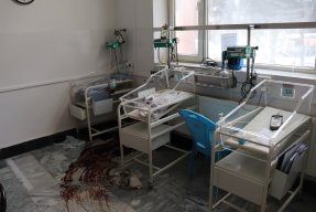Tomma sängar för nyfödda i en sjukhussal, blod på golvet.