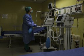 En medicinsk personal står iklädd skyddsutrustning och tittar på en monitor.