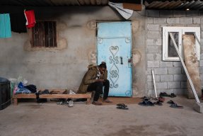 17-åriga Hassan från Sudan sitter på träbrits utanför ett hus i Libyen. 