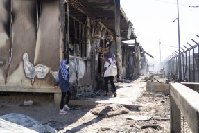 Tre personer står i det som är kvar av Morialägret på den grekiska ön Lesbos.