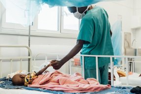 Tvååriga Sheku Kamara, som ligger på sängen på Läkare Utan Gränsers sjukhus i Kenema, Sierra Leone, håller en anställd i handen.