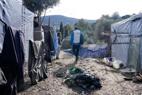 En anställd från Läkare Utan Gränser går, med ryggen mot kameran, på en grusväg genom ett läger på den grekiska ön Samos.
