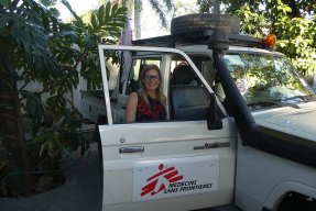 Sjuksköterskan Ulli Hedberg, som är i Haiti, står bakom en bildörr och tittar in i kameran.