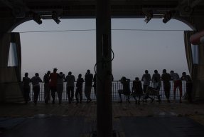 Flera människor står i motljus på däck ombord på sök- och räddningsfartyget Geo Barents och tittar ut mot havet.
