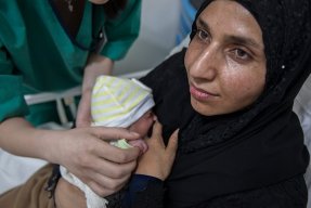 En nybliven mamma på Rafik Hariri sjukhus i Beirut, Libanon, har sitt barn tätt intill bröstet, sjukvårdpersonal står lutad över sängen med en hand på barnet.