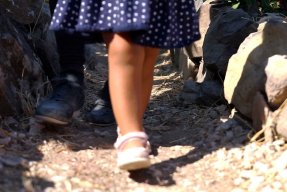 Ett barn i sandaler och klänning går på en grusstig på den grekiska ön Lesbos, endast benen syns.