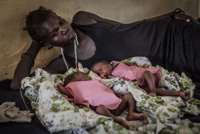 En mamma ligger på en sjukhussäng aå Aweil-sjukhuset i Sydsudan och tittar på sina nyfödda tvillingar som ligger framför henne på sängen.
