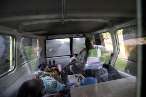 En anställd från Läkare Utan Gränser i Kongo-Kinshasa sitter bredvid en kvinna som ligger på en bår i en ambulans.