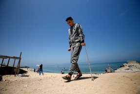En ung man går på kryckor på en strand i Gaza, Palestina.