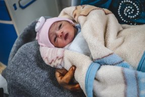 Bebisen Layth ligger på sin mammas arm på mödravårdsmottagningen al-Amal i Mosul, Irak.