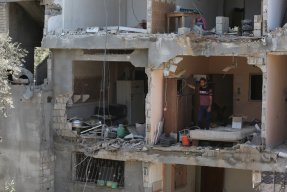Ett flervåningshus i Gaza, Palestina, som bombats. På en av våningsplanen står en man och tittar ut.