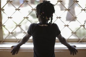 Ung kvinna står med ryggen vänd mot kameran och tittar ut genom ett fönster