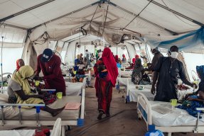 Inuti ett stort tält ligger ett tjugotal personer på sängar, både vuxna och barn.